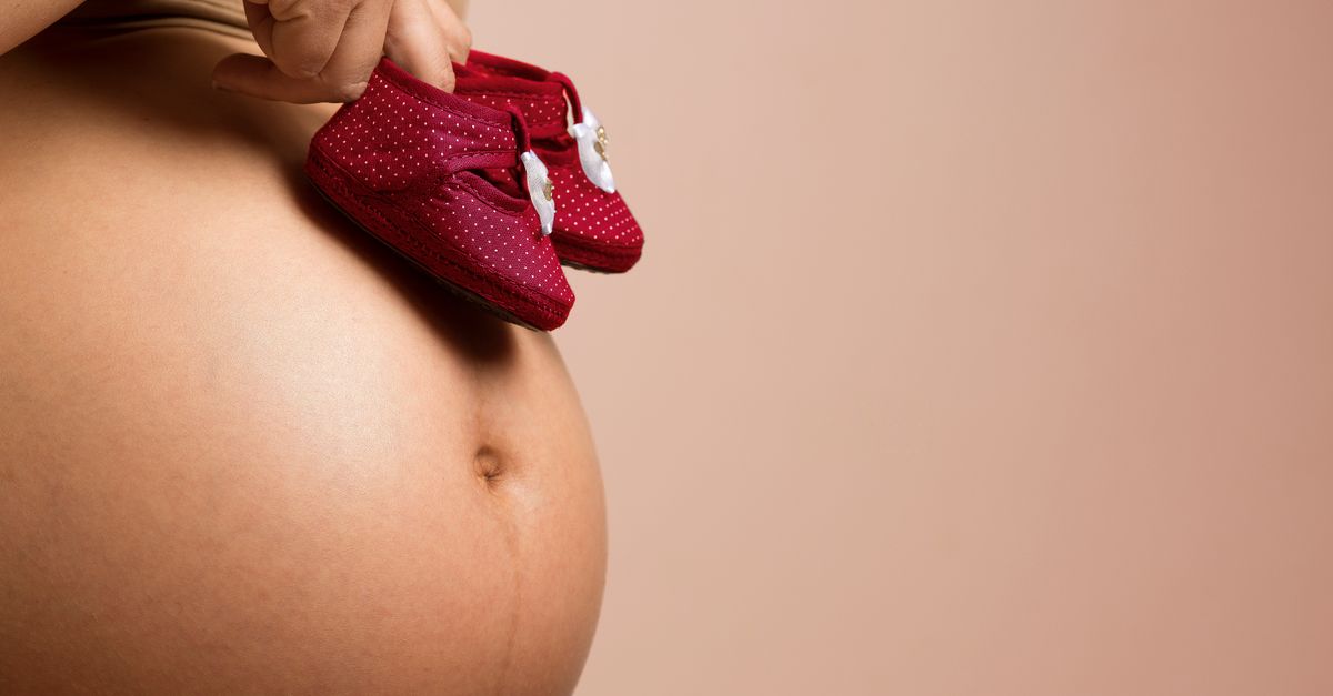 Close-up of a pregnant woman holding red baby shoes on her belly, symbolizing anticipation and love.